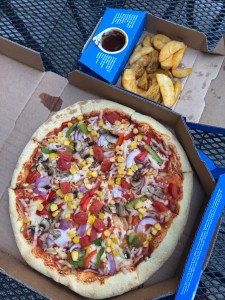 small box of potato wedges and barbecue sauce, next to a large box with a vegan pizza in