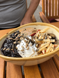 Large breakfast bowl with blueberry compote, pool of peanut butter, cream and grated apple visible, topped with seeds.