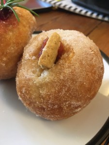 sugared doughnut with blob of light red jam and chunk of biscuit poking out on top