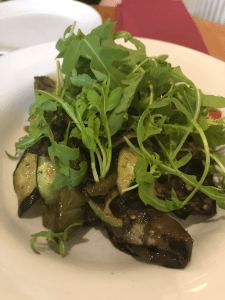 close up of plate of roasted vegetables with courgette and aubergine visible, topped with green rocket leaves.