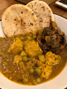 Medium sized bowl full of food. At the front, a pile of tofu and peas. At the back, two mini naan breads and an onion bhaji.