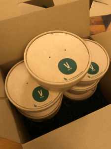 Round takeaway boxes stacked on top of each other in a large cardboard box. Green sticker on top of takeaway boxes reads 'V Giyan'