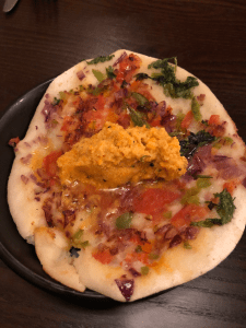 Small plate filled with a flatbread, topped with green herbs and tomato, and an orange chutney in the centre