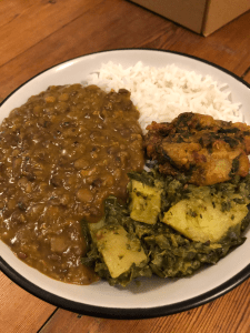 Bowl filled to the brim with basmati rice, lentil curry, saag aloo and one onion bhaji.