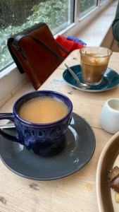 small blue china cup with tea in, small jug of oat milk, small glass with oat milk latte in. 