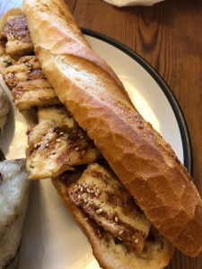 crusty white baguette with tofu slices poking out, with a sprinkling of sesame seeds