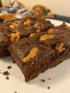 two crumbly chocolate brownies on a plate. walnut pieces are pressed into the top of the slices.