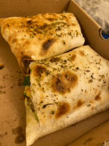 open cardboard box with folded tortilla, some char marks on top from the cooking and a sprinkling of dried herbs. Green filling of the taco is just poking out.