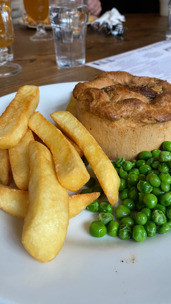 White plate with large chips and small portion of peas at the front, brown rustic looking pie at the back.