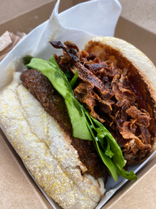 english muffin on it's side with thick crispy potato shreds visible, on top of a layer of greens and vegan patty.