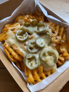 crisp waffle fries in a box, topped with liquid cheese sauce and big portion of sliced jalapeños