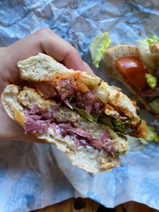 hand holding half of a burger. pink onions, green sauce and chicken style breaded patty visible inside a soft white burger bun