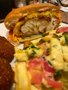 Burger cut in half to show thick cut cauliflower steak in breadcrunbs, with thick layer of melted cheese on top, lettuce beneath, sandwiched in a brioche bun.