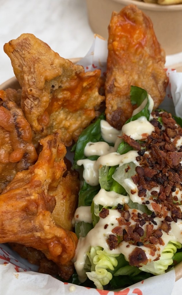 close up of dark orange crispy coated mushrooms, and lettuce drizzled with a creamy sauce and brown vegan bacon crumb