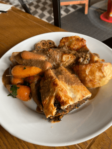 white plate piled with food - pastry, carrots and roast potato visible covered with thick dark brown gravy.